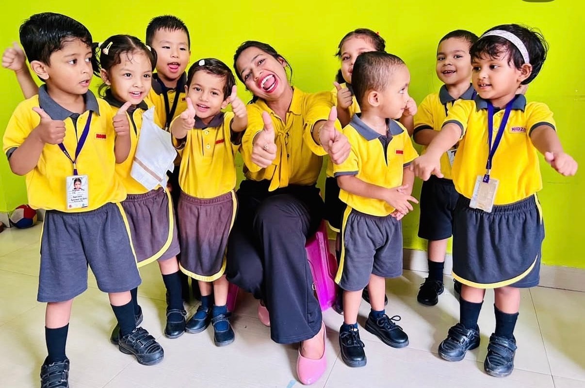 Teacher and children in yellow uniforms giving thumbs up at Kidzee Bhetapara