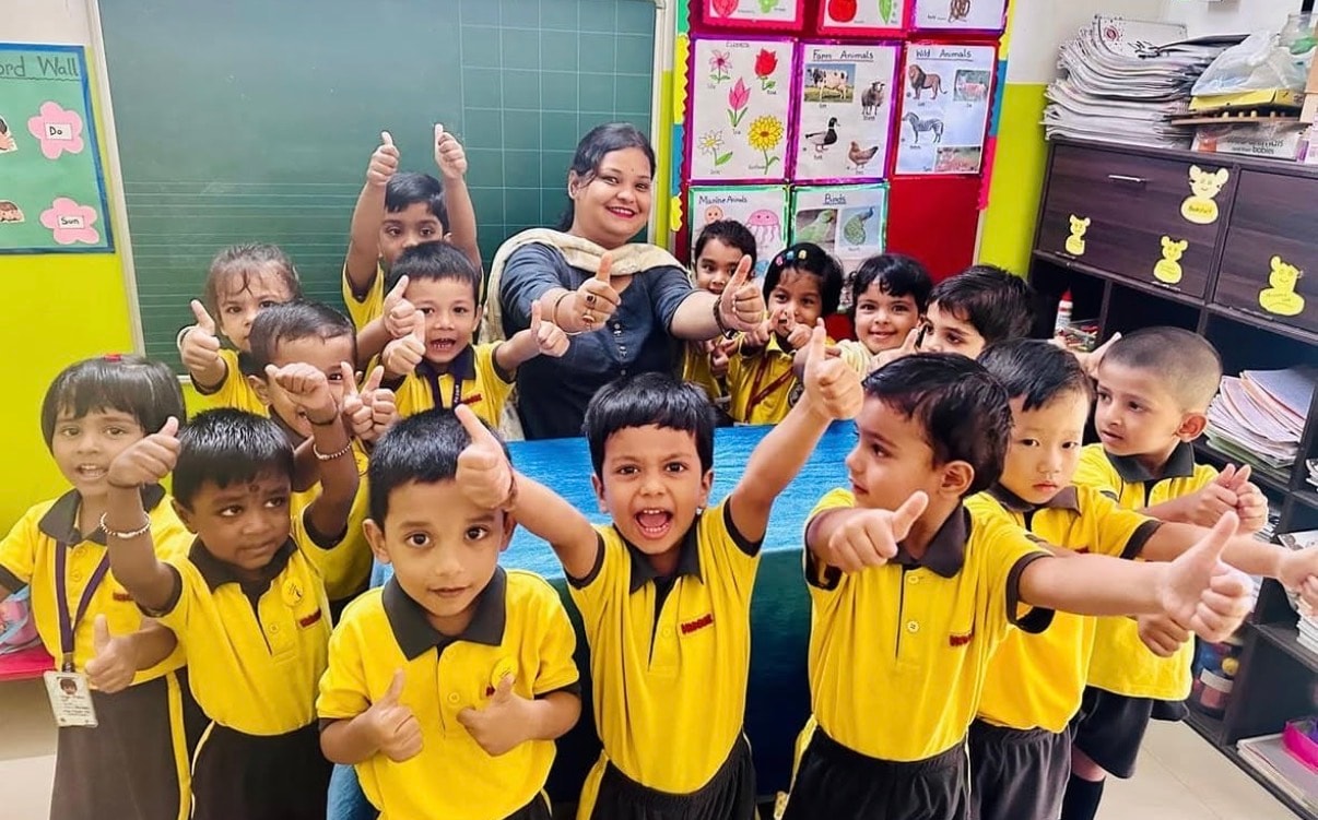 Teacher with students in yellow uniforms giving thumbs up in a decorated classroom