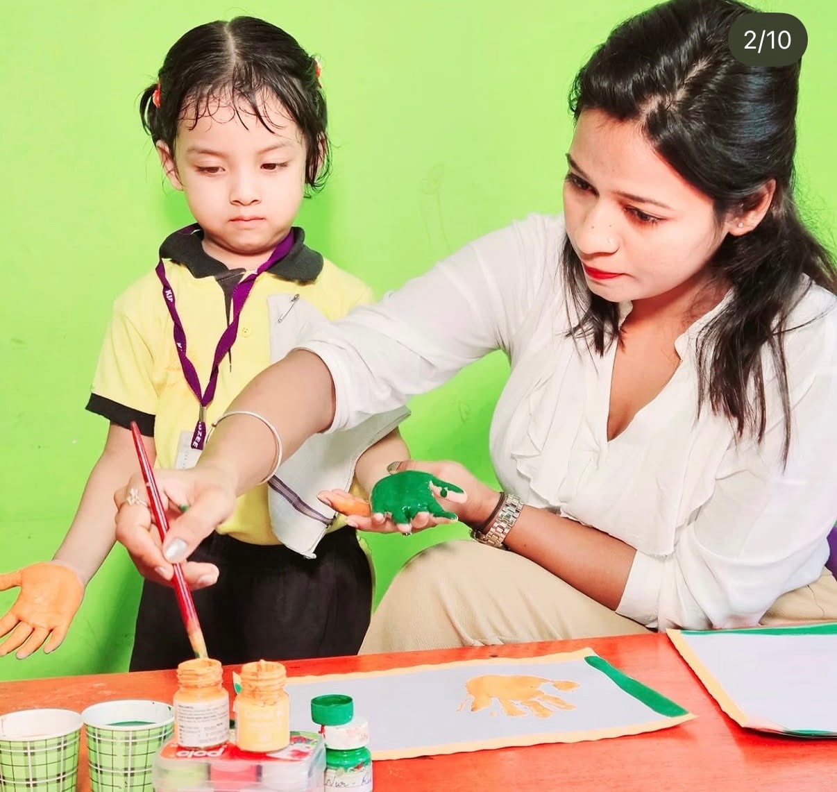 Teacher guiding a child through a painting activity at Kidzee Bhetapara